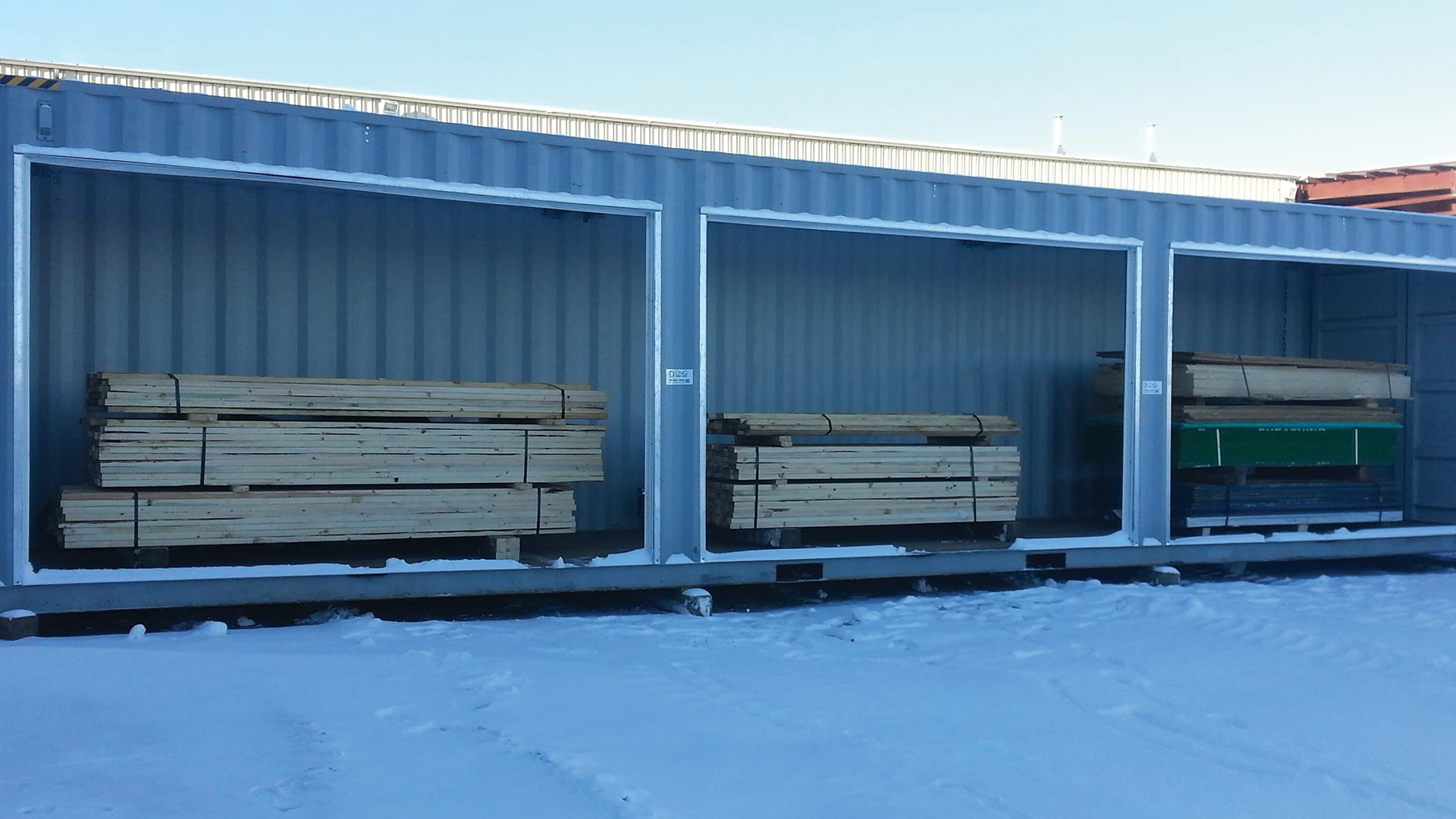 Outside of container with three bay doors open and stacks off wood inside of container